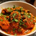 Close-up of rich, orange-red Irresistible Chicken Masala Recipe garnished with fresh cilantro in a white bowl.