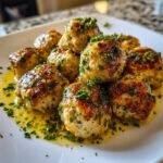A pile of golden-brown Irresistible Chicken Piccata Meatballs glistening in a lemon-butter sauce and topped with fresh parsley.