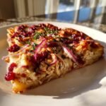 A close-up slice of Irresistible Cranberry Chicken Brie Pizza topped with red onion and thyme.