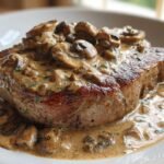 A perfectly seared pork chop smothered in rich, creamy mushroom sauce, featuring sliced mushrooms.