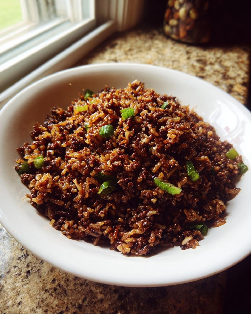 A white bowl filled with dark, savory Irresistible Dirty Rice Recipe, garnished with chopped green onions.