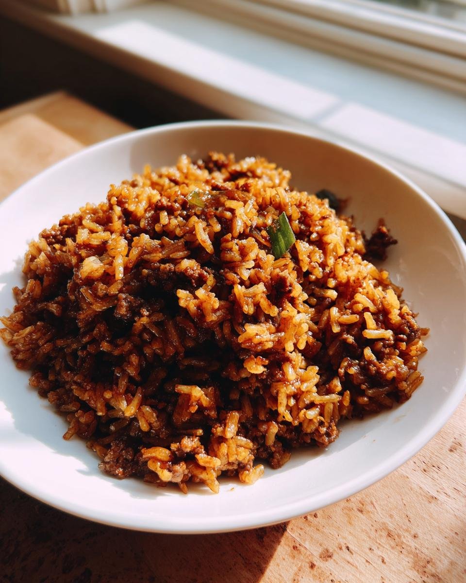 A white bowl filled with rich, brown Irresistible Dirty Rice Recipe, garnished with green onion.