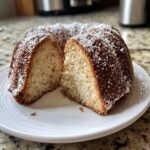 A slice cut from an Irresistible Eggnog Bundt Cake dusted with powdered sugar on a white plate.