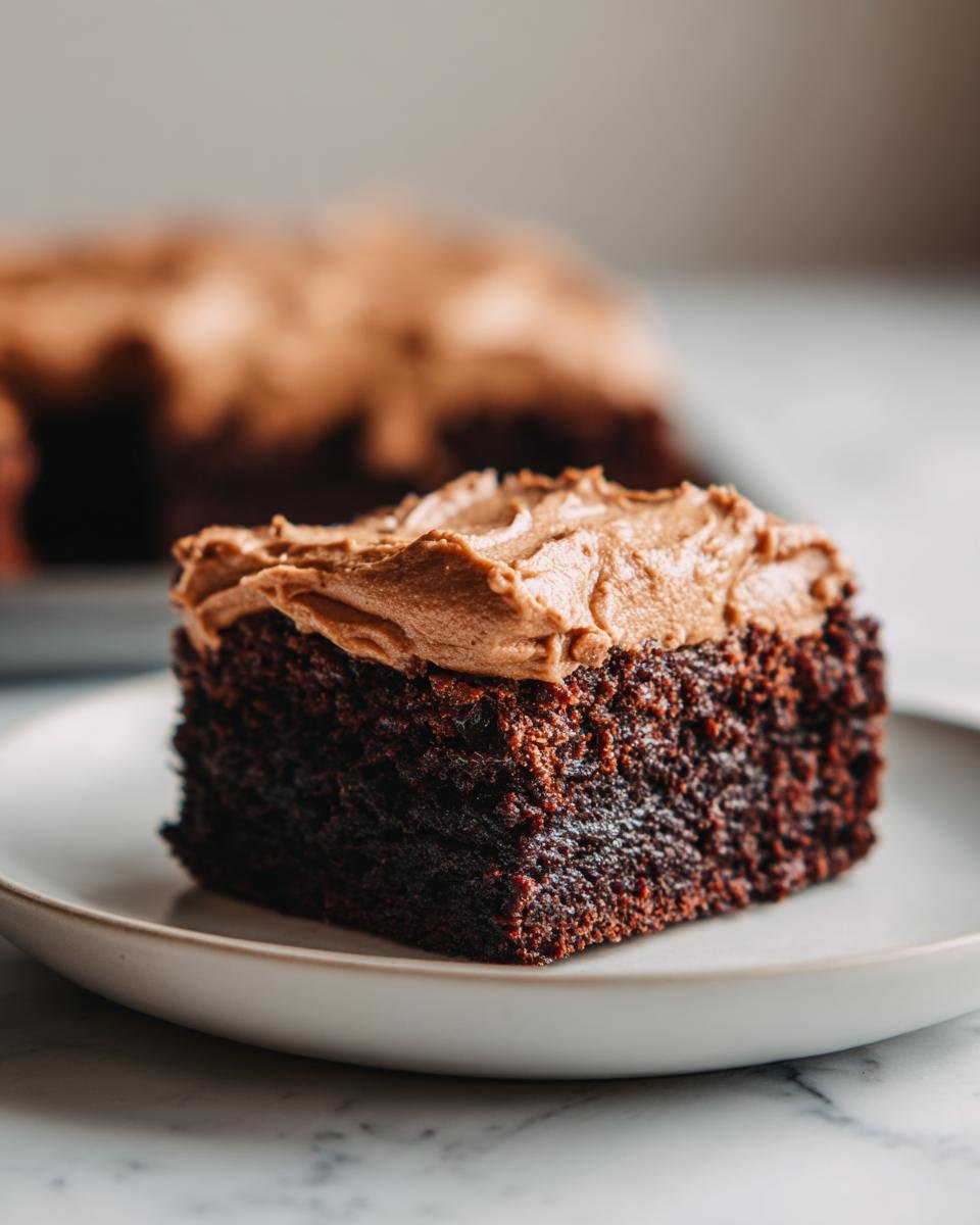 A close-up of a rich, dark slice of Irresistible Frosted Coffee Brownies topped with light brown coffee frosting.