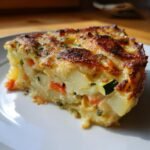A close-up slice of Irresistible Garden To Table Veggie Gratin with a golden, cheesy crust and visible layers of potatoes and carrots.