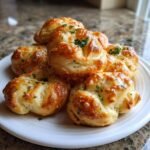 A pile of golden brown, freshly baked irresistible garlic knots topped with melted cheese and fresh parsley on a white plate.
