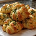 A close-up of several golden, buttery Irresistible Garlic Knots Recipe pieces topped with melted cheese and fresh parsley.