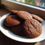A stack of dark, crinkly Irresistible Gingerbread Cookies resting on a white plate near a window.