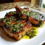 Close-up of three juicy, grilled pork chops generously topped with bright green Ladorigano sauce.