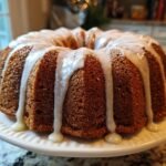A rich, brown Irresistible Holiday Spice Bundt Cake with thick white glaze dripping down the fluted sides.