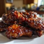 Close-up of sticky, glazed Irresistible Honey Garlic Chicken pieces piled on a white plate.