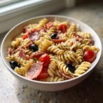 Close-up of Irresistible Italian Grinder Pasta Salad featuring rotini pasta, salami, cherry tomatoes, and black olives.