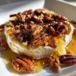 Close-up of warm, oozing baked brie topped with candied pecans and maple syrup for an Irresistible Maple Pecan Baked Brie Appetizer.
