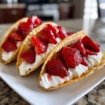 Three Irresistible Mini Strawberry Cheesecake Tacos filled with cream and fresh strawberries, served on a white plate.