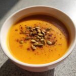 Close-up of creamy orange Irresistible Miso Pumpkin Bisque topped with toasted pepitas.