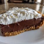 A close-up of a slice of Irresistible Nutella Cream Pie featuring a graham cracker crust, thick chocolate filling, and a generous topping of whipped cream.