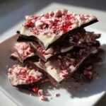 A stack of broken pieces of Irresistible Peppermint Chocolate Bark, topped with crushed candy canes.