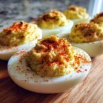 Close-up of several Irresistible Pickle Brine Deviled Eggs garnished with paprika on a wooden board.
