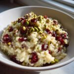 A close-up of creamy Irresistible Pistachio Cranberry Risotto topped with bright red cranberries and green pistachios.