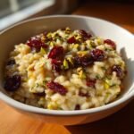 Close-up of creamy Irresistible Pistachio Cranberry Risotto topped with bright red dried cranberries and green chopped pistachios.