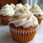 A close-up of an Irresistible Pumpkin Cupcake topped with a swirl of cream cheese frosting.