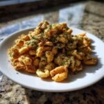 A mound of seasoned, golden Irresistible Ranch Oyster Crackers topped with green herbs on a white plate.
