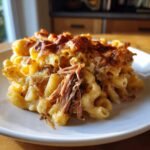 A close-up of baked macaroni and cheese topped with shredded rib cage meat, an Irresistible Rib Cage Mac Cheese Delight.