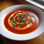 A vibrant bowl of Irresistible Roasted Tomato Basil Soup, garnished with a cream swirl and fresh basil.