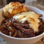 A bowl containing shredded beef, caramelized onions, melted cheese, and mashed potatoes, representing the Irresistible Savory French Onion Pot Roast Recipe.