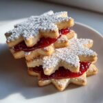 A stack of two Irresistible Snowflake Linzer Cookies filled with bright red raspberry jam and dusted with powdered sugar.