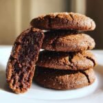 A stack of four Irresistible Soft Gingerbread Cookies, one cut in half showing the soft interior, dusted with sugar.