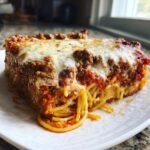 A thick, square slice of Irresistible Spaghetti Pie Comfort Food Delight topped with melted mozzarella and meat sauce.