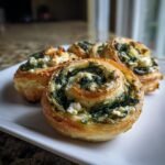 Four golden-brown Irresistible Spinach Feta Pastry Pinwheels arranged on a white plate.