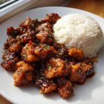 A plate of Irresistible Sweet And Spicy Thai Chicken Delight coated in a dark glaze next to a mound of white rice.