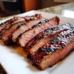 Close-up of perfectly sliced, medium-rare Irresistible Tender Grilled Marinated Flank Steak glistening with marinade.