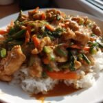 A plate of Irresistible Thai Peanut Chicken Stir Fry served over fluffy white rice, featuring chicken pieces and colorful vegetables.