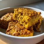 Close-up of golden square slices of Irresistible Turmeric Coconut Oat Bake in a white bowl.