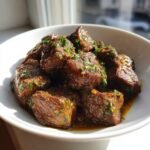 Close-up of juicy Melt In Your Mouth Garlic Butter Beef Tips coated in sauce and topped with fresh parsley in a white bowl.