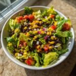 A vibrant bowl of Refreshing Mexican Salad featuring crisp lettuce, black beans, corn, diced tomatoes, and red onion.