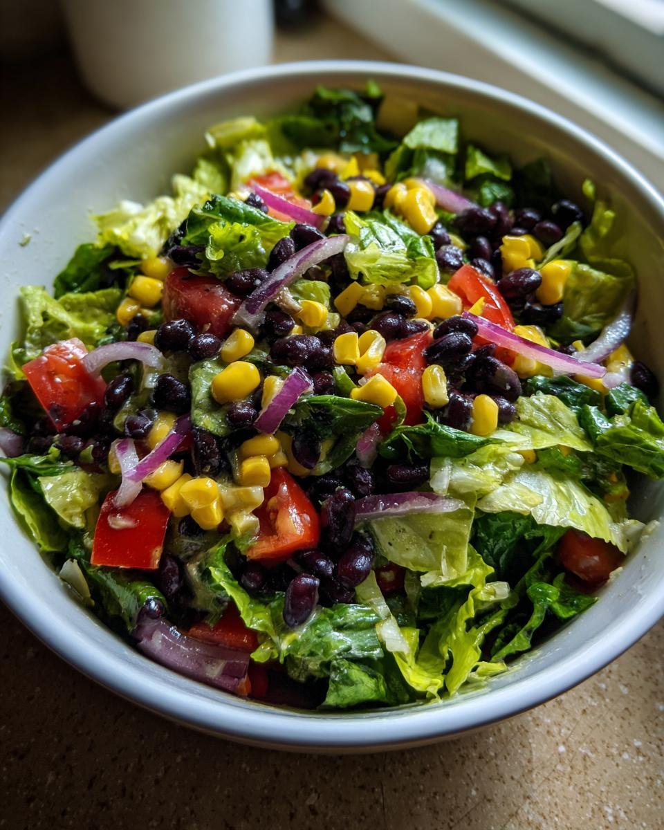 A close-up bowl of Refreshing Mexican Salad featuring lettuce, black beans, corn, tomatoes, and red onion.