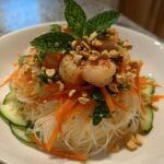 A bowl of Refreshing Spring Roll Salad featuring vermicelli noodles, shrimp, shredded carrots, cucumbers, and crushed peanuts.