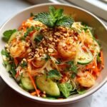 Close-up of a bowl of Refreshing Spring Roll Salad With Spicy Ginger Dressing, topped with shrimp, peanuts, and mint.
