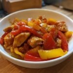 Close-up of Savory Basque Chicken And Peppers Recipe Youll Love served in a white bowl on a wooden surface.