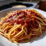 Close-up of spaghetti topped with rich, homemade marinara sauce and dried herbs.