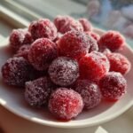 A close-up of Sparkling Sugared Cranberries piled on a small white plate, glistening in the sunlight.
