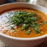 Close-up of a bowl of creamy, orange Irresistible Thai Coconut Red Lentil Soup topped with fresh chopped cilantro.